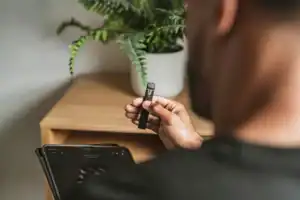一名穿深色上衣的人手持外觀似電子煙的細長裝置，旁邊放著平板電腦。